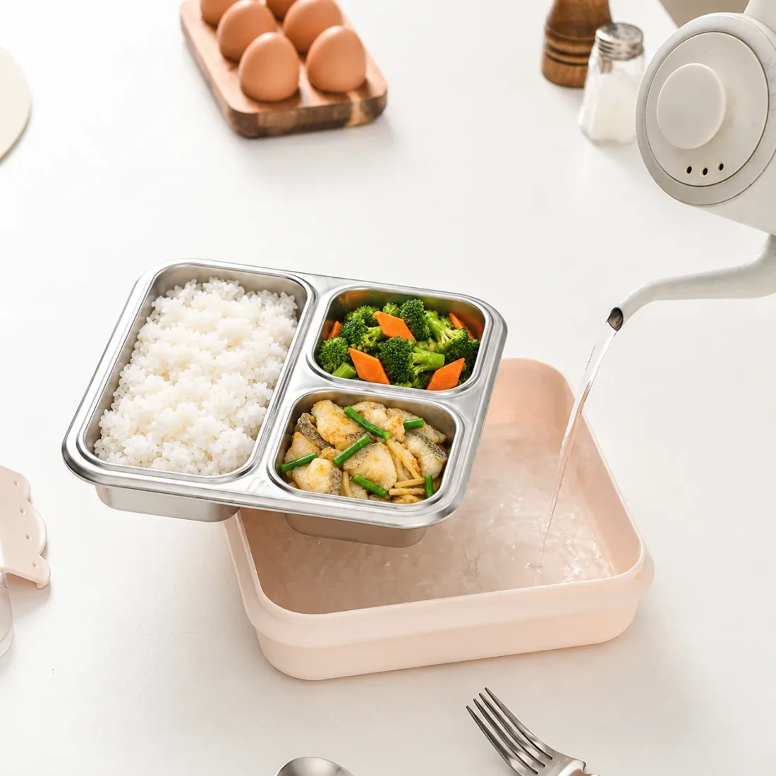 示意图:水壶往粉色饭盒底座里倒热水,不锈钢内胆提在底座上方,里面是米饭、西兰花胡萝卜、煎鱼片